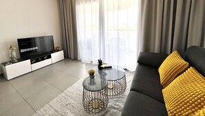 A modern living room with a sofa, a coffee table, a TV, and a balcony view. - 127 NIC - Stay Sun Line Apartment (Nicosia)