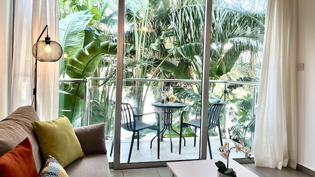 A room with a sofa, a table, and a balcony with chairs and a small table. - 122 PRO - Stay Tropical Apartment (Paralimni)