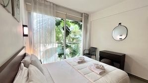 A hotel room with a bed, a desk, a chair, a large window with curtains, and a wall-mounted mirror. - 122 PRO - Stay Tropical Apartment (Paralimni)