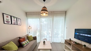 A living room with a sofa, a coffee table, a TV, and a window with curtains. - 122 PRO - Stay Tropical Apartment (Paralimni)