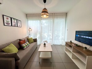 A living room with a sofa, a coffee table, a TV, and a window with curtains. - 122 PRO - Stay Tropical Apartment (Paralimni)