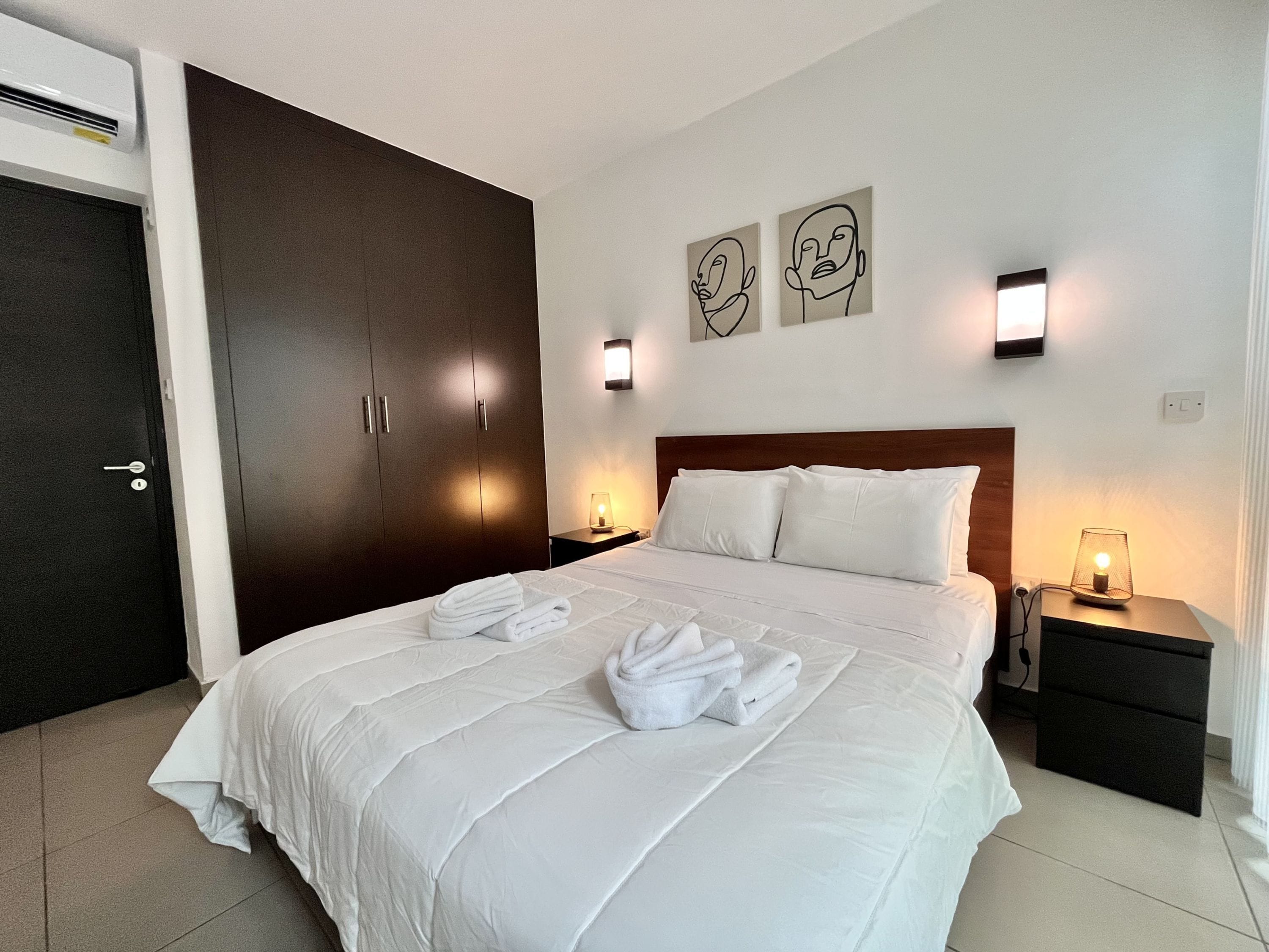 A hotel room with a bed, two bedside tables, a wardrobe, and artwork on the wall.