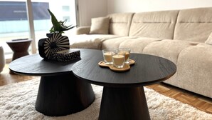 Una sala de estar moderna con un sofá, dos mesas redondas, una planta en maceta y velas.