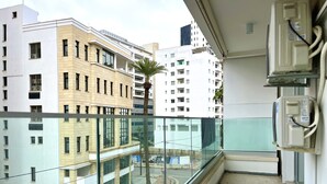 Un balcón con vistas a un paisaje urbano, que incluye edificios de varios pisos y una palmera.