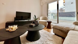 Una sala de estar moderna con un televisor de pantalla plana, una mesa redonda, un sofá y un amplio ventanal con vistas a edificios.