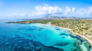 Luftaufnahme einer Küstenstadt mit klarem türkisblauem Wasser, einem Strand und einem gebirgigen Hintergrund.