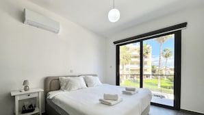 Ett modernt hotellrum med en stor säng, ett sängbord med en lampa och utsikt över ett bostadsområde genom ett stort fönster.