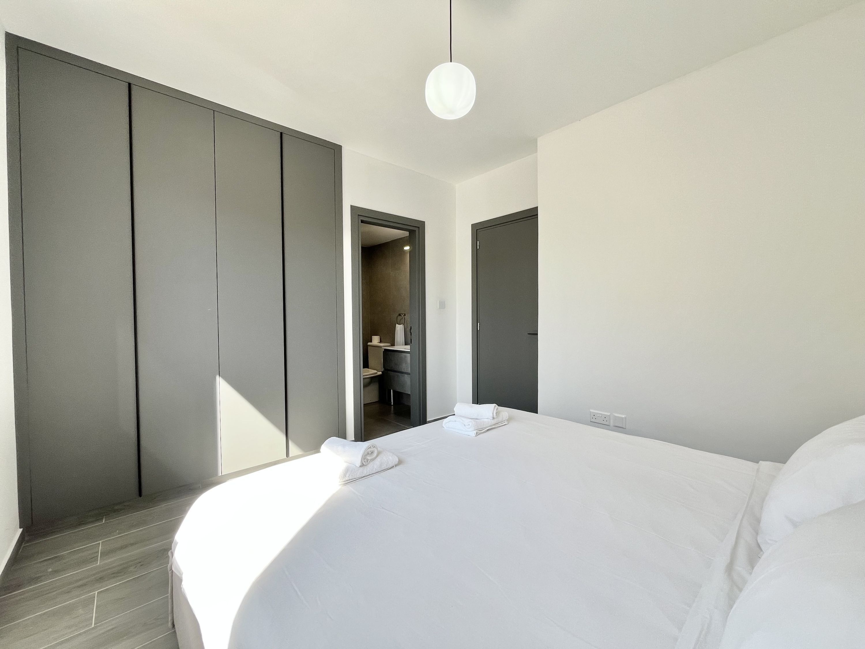 Une chambre d’hôtel moderne avec un grand lit, une armoire et une salle de bain visible à travers une porte ouverte.