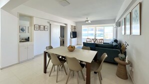 A spacious living area with a dining table, chairs, a sofa, and a TV. - 39 LCA - Stay Makenzie View Apartment (Larnaca)