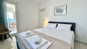 A hotel room with a bed, a chair, a table, and a view of the sea. - 39 LCA - Stay Makenzie View Apartment (Larnaca)