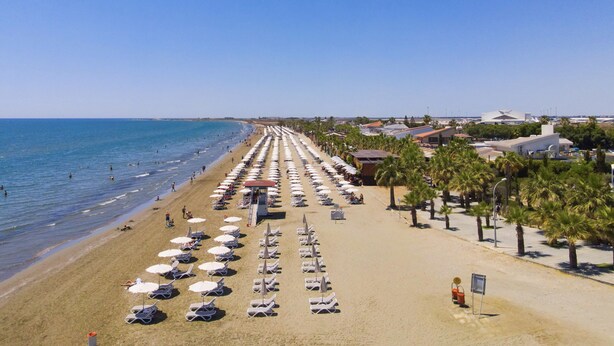 A beach with rows of sun loungers and umbrellas, a clear sky, and a calm sea. - 39 LCA - Stay Makenzie View Apartment (Larnaca)
