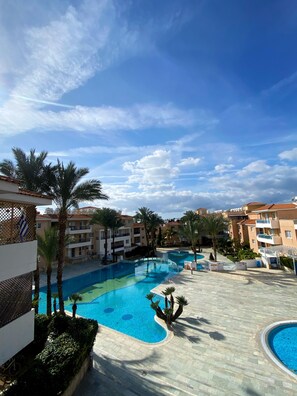 A resort with a large swimming pool, palm trees, and multi-story buildings. - 43 PAP - Stay Iris Apartment (Paphos)