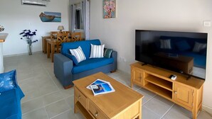Una sala de estar con sofá, mesa de centro, televisión, ventilador de techo, comedor y obras de arte.