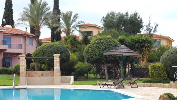 Piscina con sillas de descanso, rodeada de vegetación y edificios.