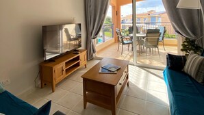 Una sala de estar con televisor, mesa de centro de madera, sofá azul y ventilador de techo.