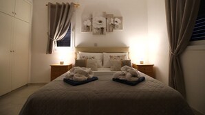 Un dormitorio con una cama, dos mesitas de noche, un ventanal con cortinas, una obra de arte colgada en la pared y un armario.