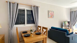 Comedor con una mesa preparada para cuatro personas, un ventilador de techo y un sofá al fondo.