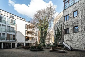 Um pátio com uma árvore central, edifícios com varandas e um caminho de tijolos.