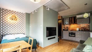 Un espacio habitable compacto con cama, televisor, zona de comedor y kitchenette.