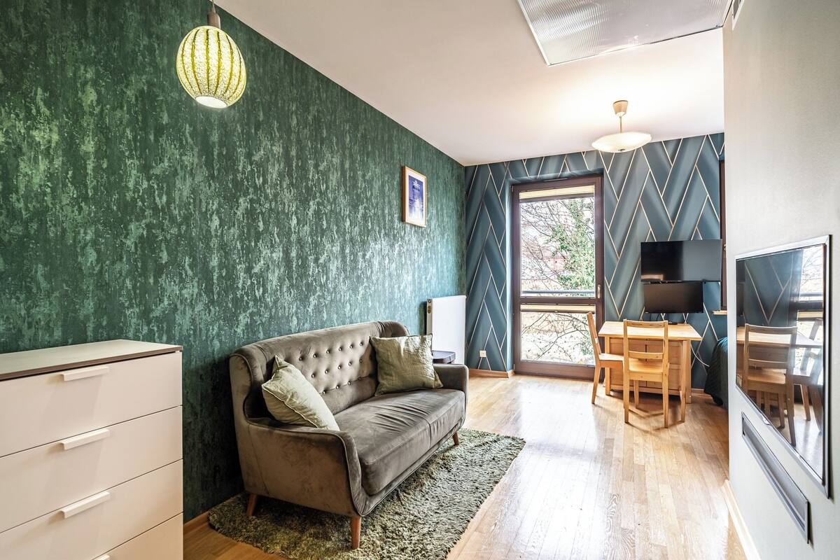 A room with a green textured wall, a tufted sofa, a wooden dining table, and a television.
