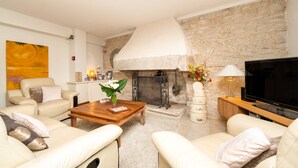 A living room with a stone fireplace, a flat-screen TV, and a sofa. - Room 'Chambre Campagne' with Shared Pool, Shared Terrace and Wi-Fi (Saint-Avé)