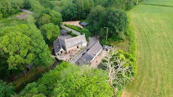 Vue aérienne d’une propriété comprenant un bâtiment principal, une allée et des espaces verts environnants.