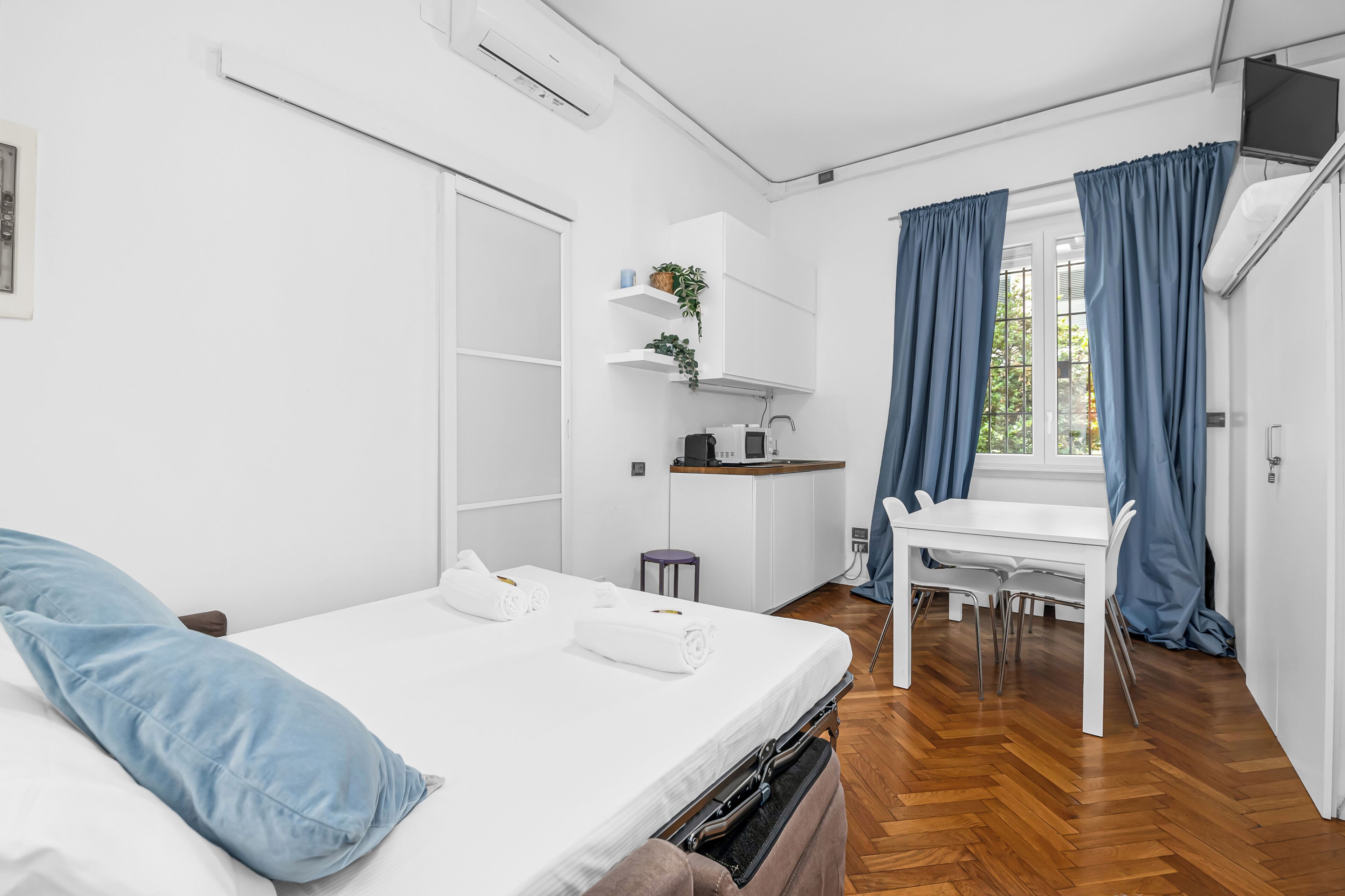Ein modernes Hotelzimmer mit einem Bett, einem Schreibtisch, einem Stuhl, einem kleinen Tisch, einer Pflanze und einem Fenster mit Vorhängen.