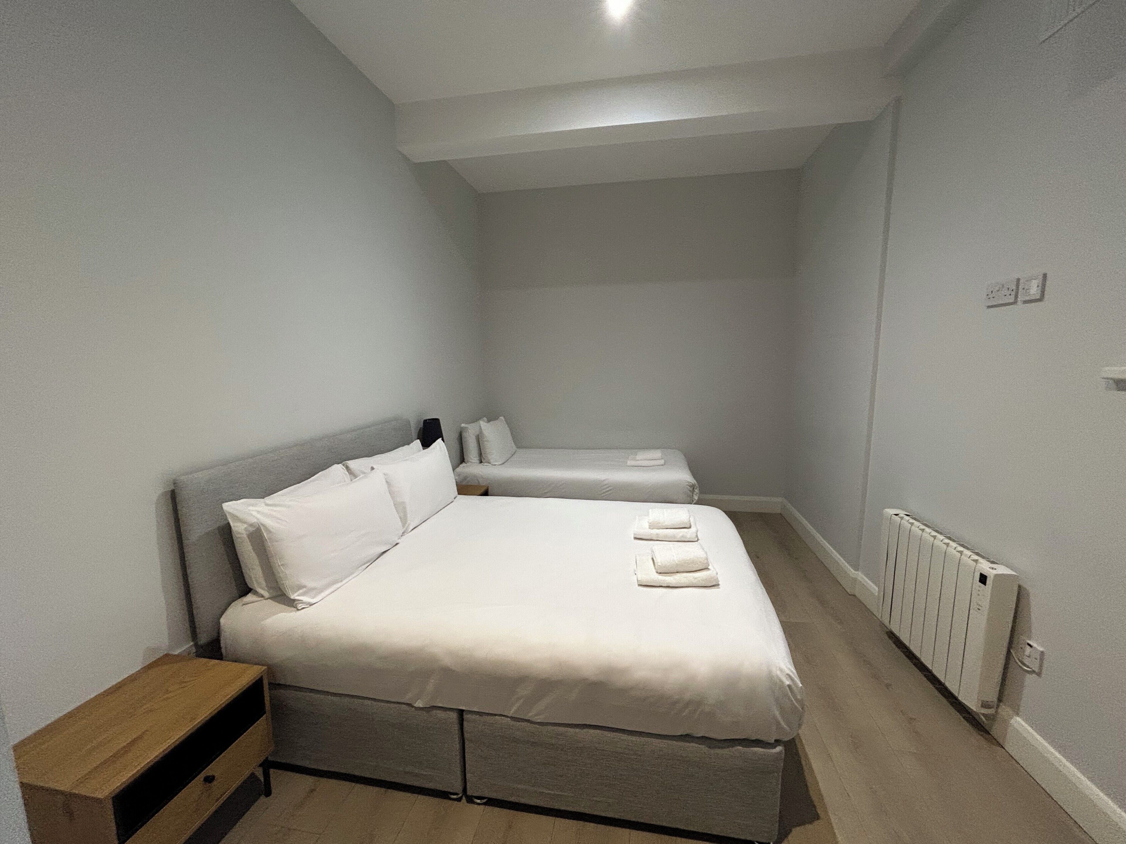 A small, clean room with a single bed, a bedside table, and a radiator.