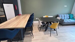 Un espace de vie moderne avec une table à manger en bois, des chaises bleues et jaunes, un canapé gris et un mur d’accent vert.