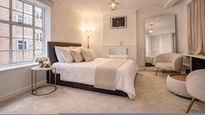 A bedroom with a bed, bedside table, lamp, chair, and a large window. - Luxury Pad for Couples Next to Paddington Station (London)