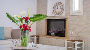 Una sala de estar con chimenea, un reloj y un florero con flores.