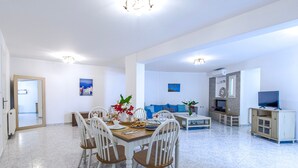 Amplia sala de estar con mesa de comedor, sillas, sofá, televisor y chimenea.