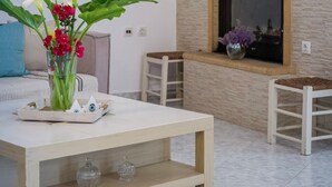 Un salón con un sofá blanco, una mesa de centro de madera con un jarrón de flores, una chimenea y un reloj de pared.