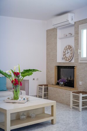 Ein Wohnzimmer mit einem weißen Sofa, einem Holztisch mit Blumenvase, einem Kamin und einer Wanduhr.