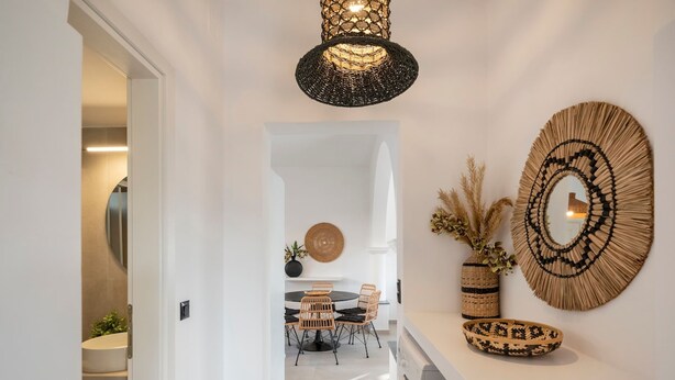 A hallway with a washing machine, a dining area with chairs and a table, and a wall with decorative items. - Haven in Naousa (Paros)