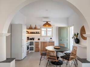 Una cucina moderna con mobili bianchi, un'area pranzo con sedie in vimini e un'ampia finestra.