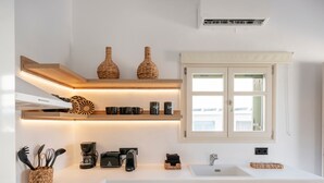 A modern kitchen with white cabinetry, wooden shelves, and a built-in stove. - Haven in Naousa (Paros)