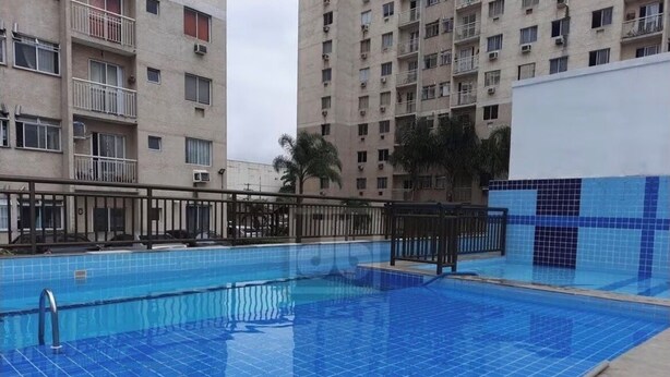 Une piscine aux carreaux bleus, entourée d’une rambarde en métal et située à côté d’un immeuble de grande hauteur.