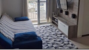 Une chambre avec un lit, une télévision, une armoire et un balcon offrant une vue sur la ville.