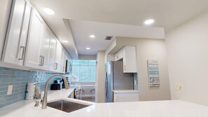 A modern kitchen with white cabinets, a stainless steel sink, and a blue-tiled backsplash. - Tivoli 5227 | New to Listing Golf Views, Pool, 6-Seater Golf Cart (Miramar Beach)