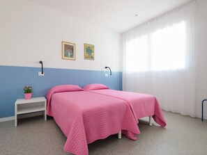 A bedroom with two beds, a nightstand, a potted plant, and two wall-mounted lamps. - Vibrant Property in Lignano (Lignano Sabbiadoro)