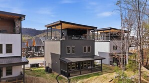 Una casa moderna de varios pisos con un espacio exterior cubierto, un balcón y vistas del paisaje circundante.