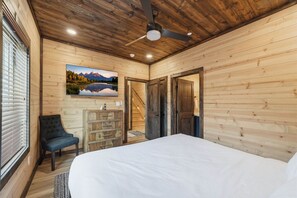 Una habitación con paneles de madera, una cama, una silla, un tocador y un cuadro en la pared.