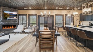 A modern kitchen with a central island, a dining area with a fireplace, and large windows with blinds. - NEW Build - Smokies Haven w/ Hot Tub, Games, MORE (Pigeon Forge)