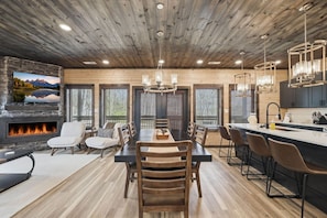 A modern kitchen with a central island, a dining area with a fireplace, and large windows with blinds. - NEW Build - Smokies Haven w/ Hot Tub, Games, MORE (Pigeon Forge)