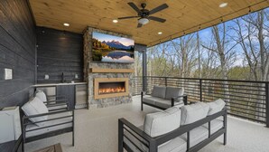 A covered outdoor area with a stone fireplace, seating, and a view of trees. - NEW Build - Smokies Haven w/ Hot Tub, Games, MORE (Pigeon Forge)