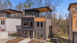 A modern multi-story building with a covered outdoor seating area, a staircase, and a small garden. - NEW Build - Smokies Haven w/ Hot Tub, Games, MORE (Pigeon Forge)