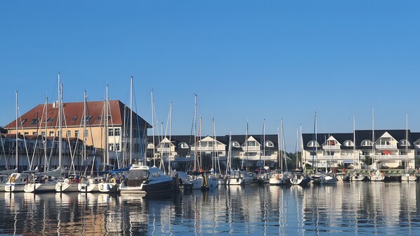 A marina with multiple boats docked, a building with a red roof, and a clear blue sky.