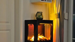 Une pièce d’angle avec un poêle à bois noir, une étagère blanche remplie de livres et un rideau.