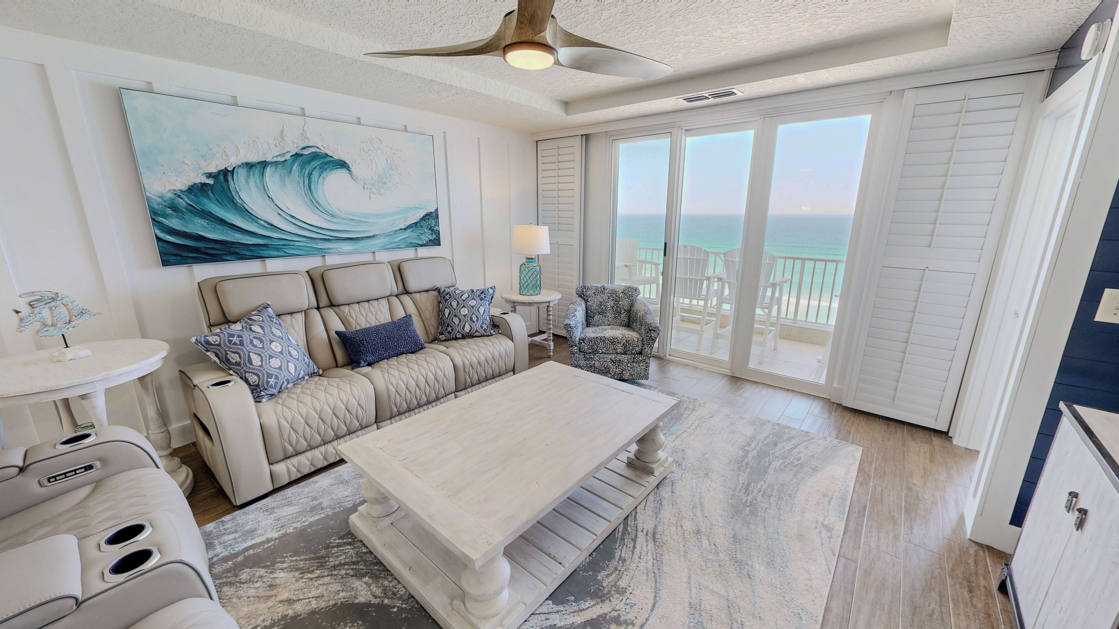 A spacious living area with a large window overlooking the ocean, a ceiling fan, and a cozy seating arrangement.